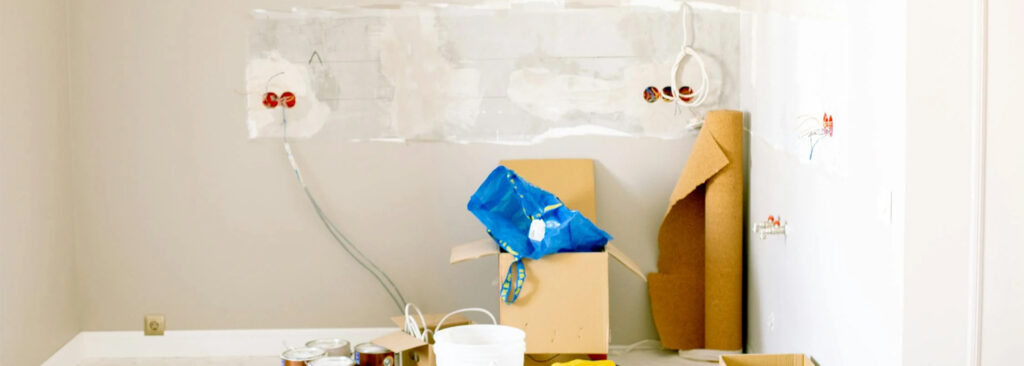 Unfinished room with paint supplies, cardboard boxes, and exposed wiring on white walls.
