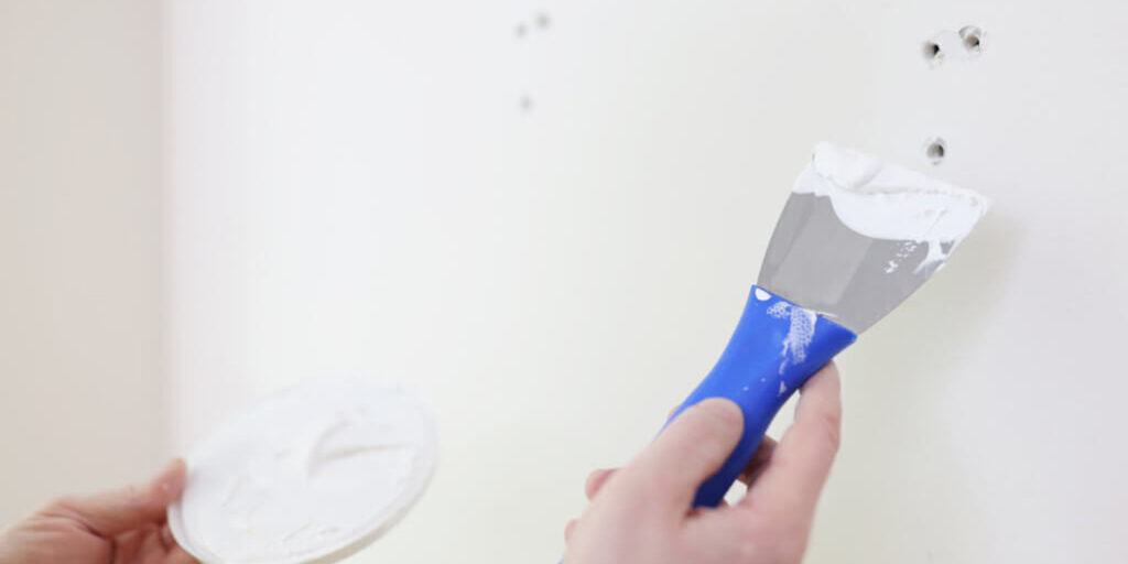 Applying wall filler with a putty knife to small holes.