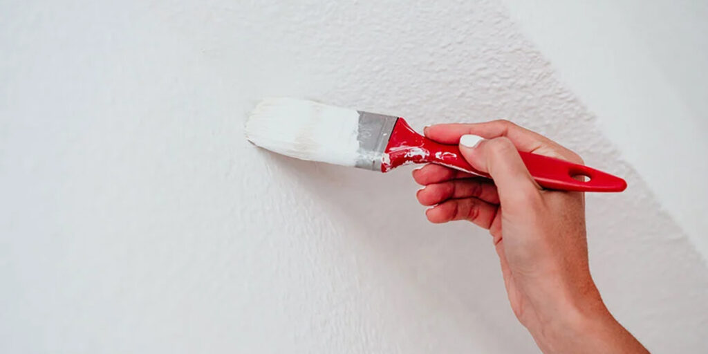White paint being applied with a brush to a wall corner.