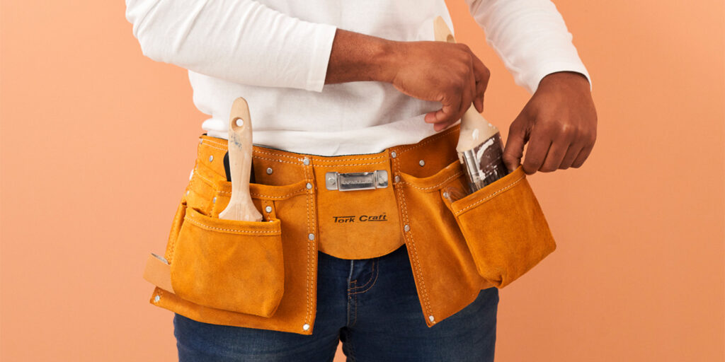 Person wearing a painting toolbelt filled with paintbrushes and supplies.